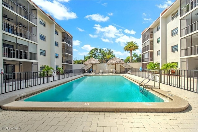 pool with fence, a ceiling fan, and a patio