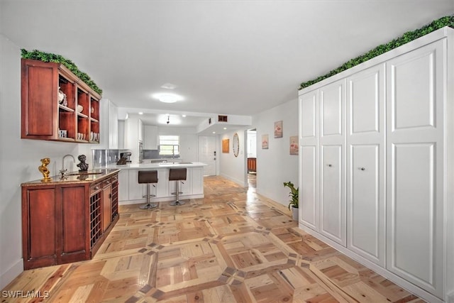 kitchen with a peninsula, a sink, light countertops, open shelves, and a kitchen bar