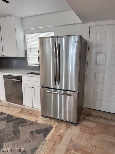 kitchen featuring stainless steel appliances, backsplash, white cabinets, and light wood-type flooring