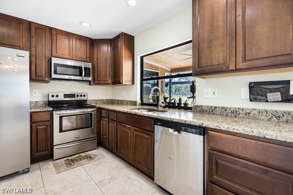 kitchen with sink, dark brown cabinets, stainless steel appliances, light stone counters, and light tile patterned floors