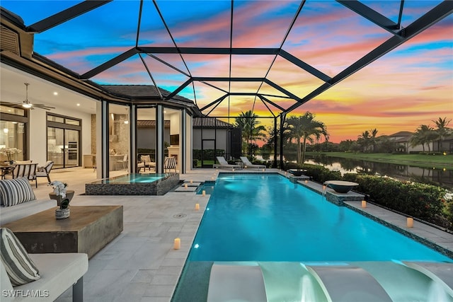 pool at dusk with a patio, a water view, an in ground hot tub, and glass enclosure