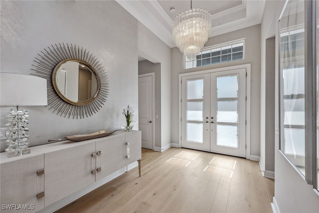 foyer featuring light wood-type flooring, an inviting chandelier, a raised ceiling, ornamental molding, and french doors