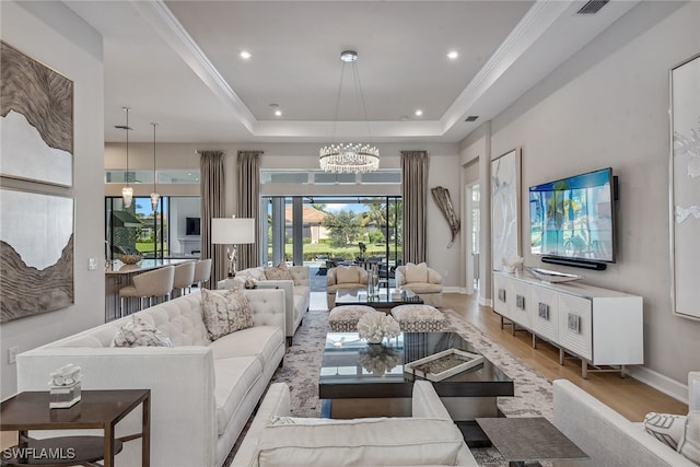 living room featuring ornamental molding, an inviting chandelier, a tray ceiling, and light hardwood / wood-style floors