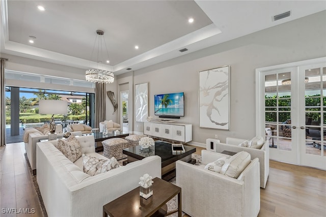 living room featuring light hardwood / wood-style flooring, a tray ceiling, and plenty of natural light