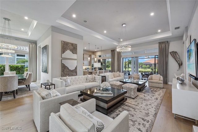 living room featuring a raised ceiling, light wood-type flooring, and a chandelier