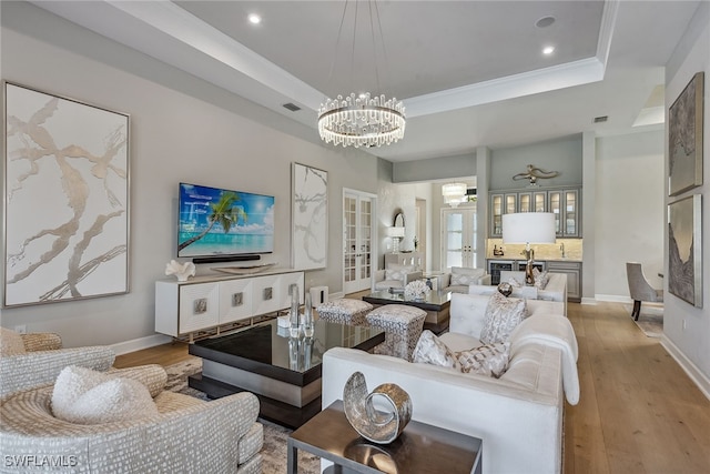 living room featuring light wood-type flooring, a raised ceiling, crown molding, and an inviting chandelier