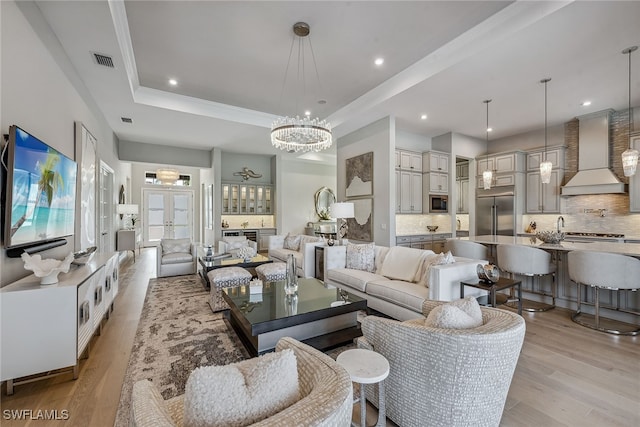 living room with an inviting chandelier, light hardwood / wood-style floors, a raised ceiling, and crown molding