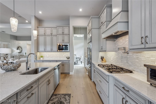 kitchen featuring light stone counters, pendant lighting, premium range hood, sink, and stainless steel appliances