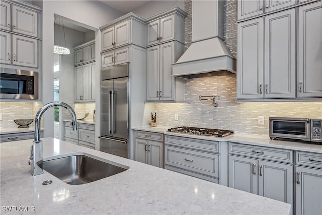 kitchen featuring sink, decorative light fixtures, backsplash, built in appliances, and custom range hood