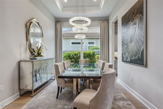 dining area with a notable chandelier, ornamental molding, a raised ceiling, and hardwood / wood-style floors