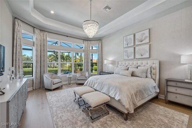 bedroom with an inviting chandelier, light hardwood / wood-style flooring, a tray ceiling, and multiple windows