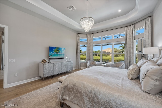 bedroom with ornamental molding, a raised ceiling, a chandelier, and light hardwood / wood-style flooring