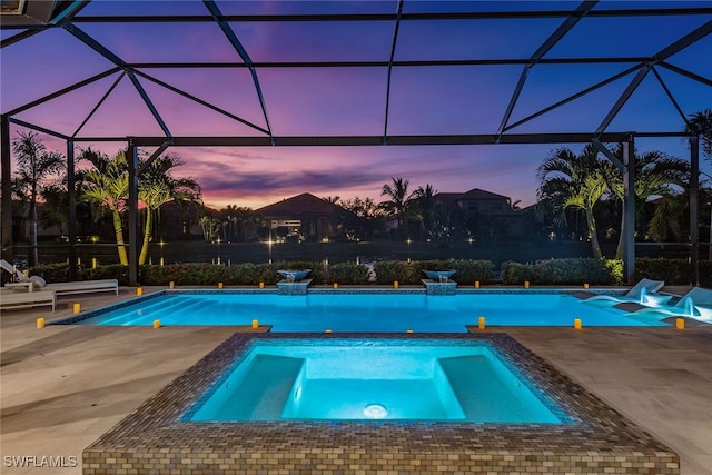 pool at dusk featuring glass enclosure, an in ground hot tub, and a patio