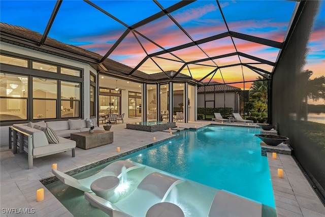 pool at dusk with glass enclosure, outdoor lounge area, and a patio