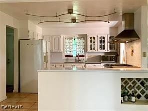 kitchen featuring wall chimney exhaust hood, stainless steel appliances, white cabinetry, and light tile patterned flooring