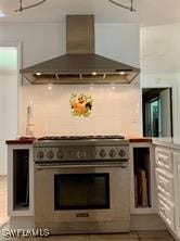 kitchen with stainless steel range, wall chimney range hood, and white cabinetry