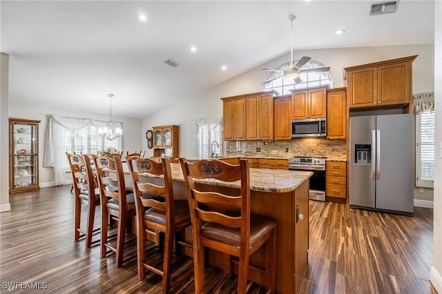 kitchen featuring light stone counters, stainless steel appliances, brown cabinetry, a kitchen bar, and pendant lighting