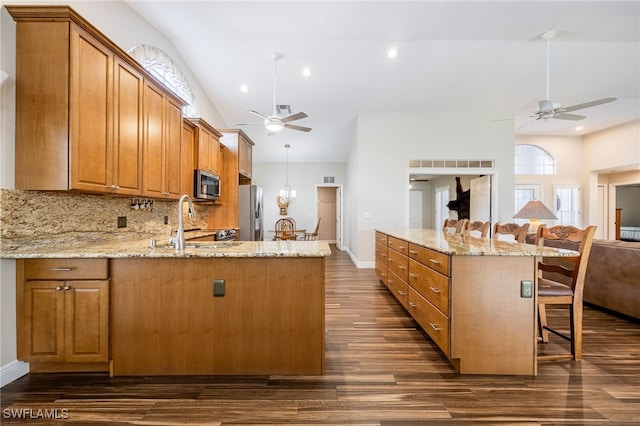 kitchen featuring light stone counters, appliances with stainless steel finishes, open floor plan, and a sink