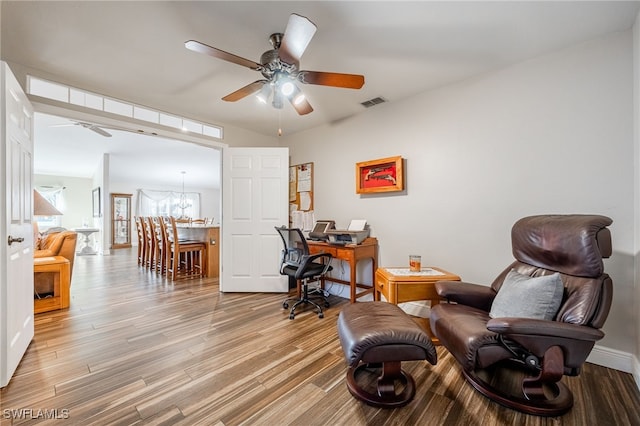 living area with ceiling fan with notable chandelier, visible vents, baseboards, and wood finished floors