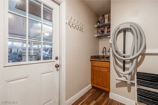 doorway to outside with dark wood-type flooring, indoor wet bar, a sink, and baseboards