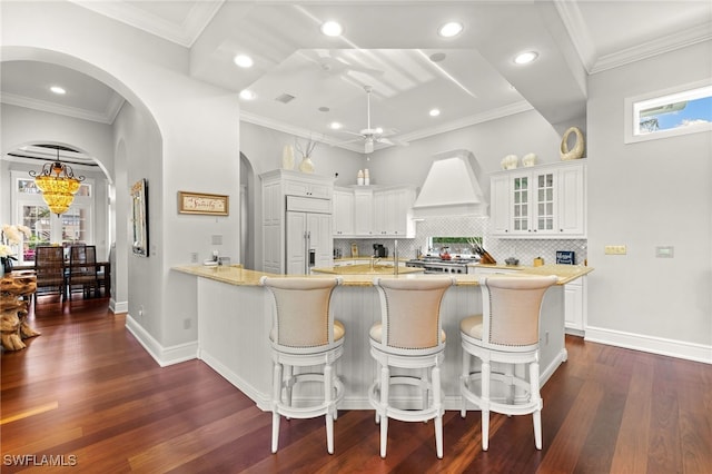 kitchen with a kitchen breakfast bar, paneled built in fridge, crown molding, dark hardwood / wood-style flooring, and white cabinetry