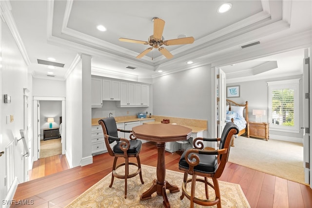 dining area with ceiling fan, a raised ceiling, ornamental molding, and light hardwood / wood-style flooring