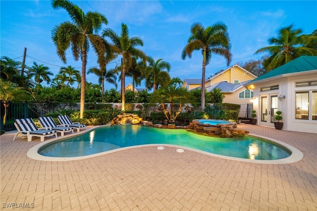 pool at dusk with an in ground hot tub and a patio