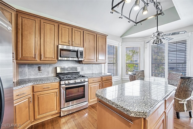 18141 Old Pelican Bay Dr, Fort Myers Beach, FL 33931 - kitchen with appliances with stainless steel finishes, lofted ceiling, light wood-style flooring, brown cabinetry, and tasteful backsplash