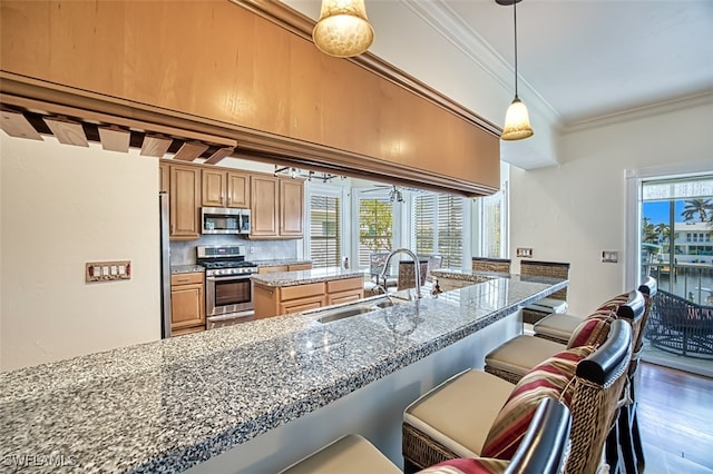 18141 Old Pelican Bay Dr, Fort Myers Beach, FL 33931 - kitchen featuring stainless steel appliances, crown molding, a breakfast bar area, light stone countertops, and wood finished floors