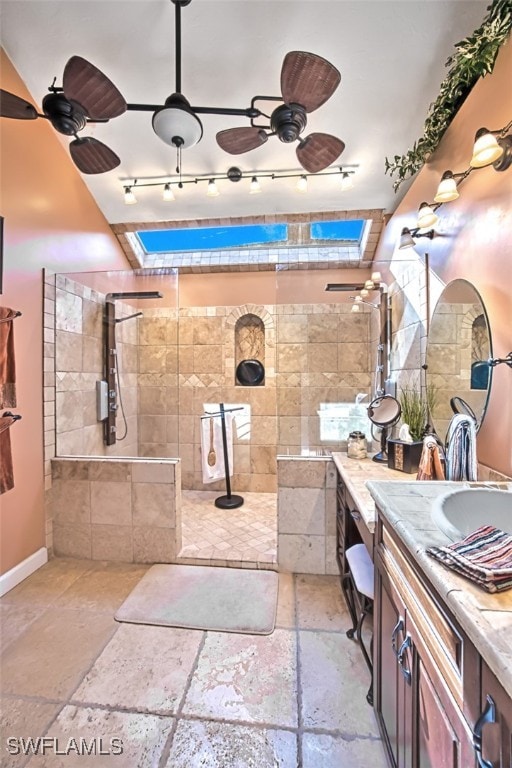 bathroom with a skylight, ceiling fan, vanity, and tiled shower