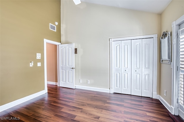 unfurnished bedroom with a towering ceiling, dark wood-type flooring, and a closet