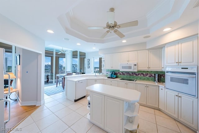 kitchen featuring kitchen peninsula, white appliances, a center island, and a tray ceiling