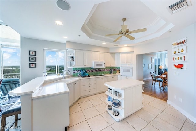 kitchen with a raised ceiling, white appliances, a kitchen island, and ceiling fan