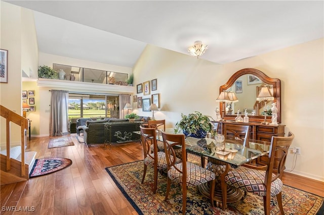 dining space featuring hardwood / wood-style floors, stairway, baseboards, and high vaulted ceiling