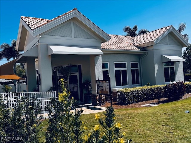 view of front of home with covered porch, stucco siding, a tiled roof, and a front yard