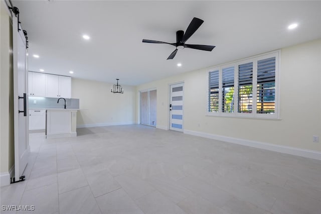 empty room with sink, ceiling fan with notable chandelier, and a barn door