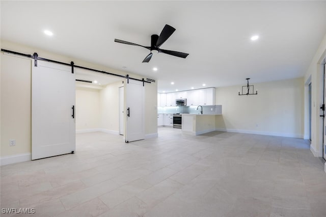 unfurnished living room with a barn door, sink, and ceiling fan