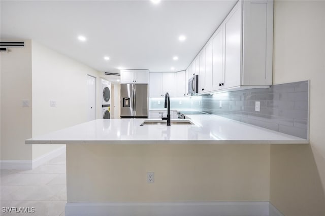 kitchen featuring stainless steel appliances, white cabinets, kitchen peninsula, and stacked washer and clothes dryer