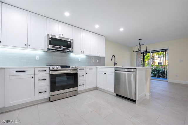 kitchen with white cabinets, kitchen peninsula, appliances with stainless steel finishes, a notable chandelier, and decorative backsplash