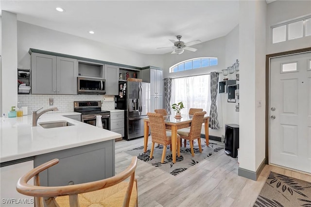 kitchen featuring kitchen peninsula, appliances with stainless steel finishes, gray cabinetry, ceiling fan, and sink