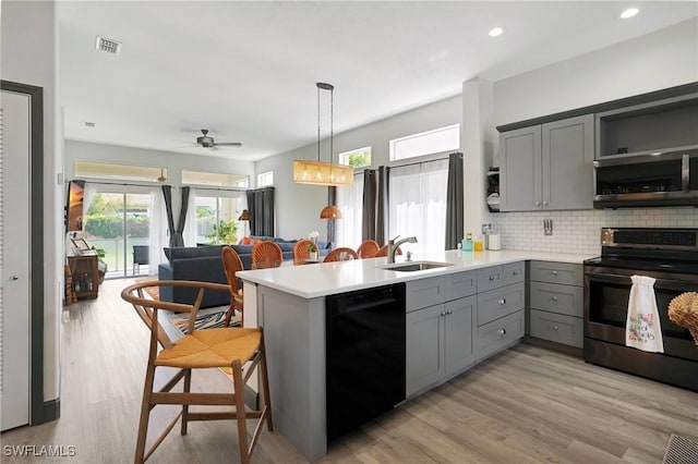 kitchen featuring sink, gray cabinets, appliances with stainless steel finishes, decorative light fixtures, and kitchen peninsula