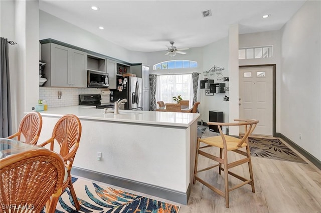 kitchen featuring sink, tasteful backsplash, kitchen peninsula, appliances with stainless steel finishes, and light wood-type flooring