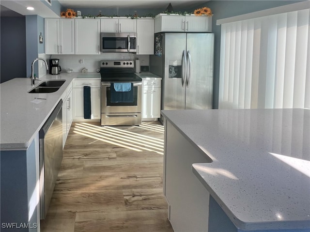 kitchen featuring appliances with stainless steel finishes, tasteful backsplash, white cabinets, light stone countertops, and sink