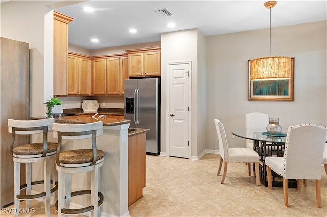 kitchen featuring light tile patterned floors, a breakfast bar, dark stone countertops, stainless steel refrigerator with ice dispenser, and decorative light fixtures