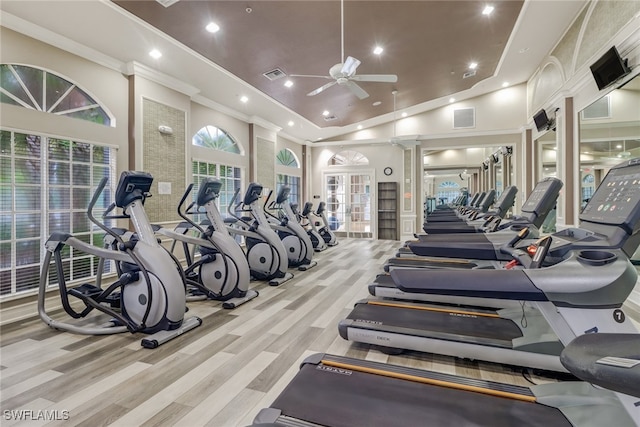 workout area featuring a high ceiling, ornamental molding, decorative columns, light wood-type flooring, and ceiling fan