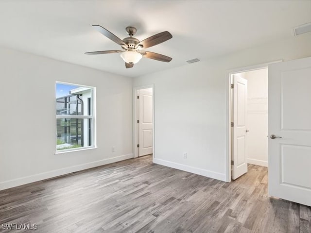 unfurnished bedroom with ceiling fan, a closet, a spacious closet, and light hardwood / wood-style floors