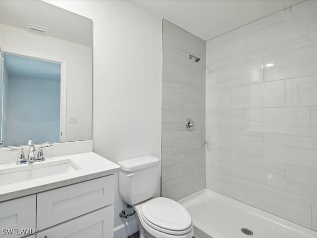 bathroom with toilet, tiled shower, and vanity