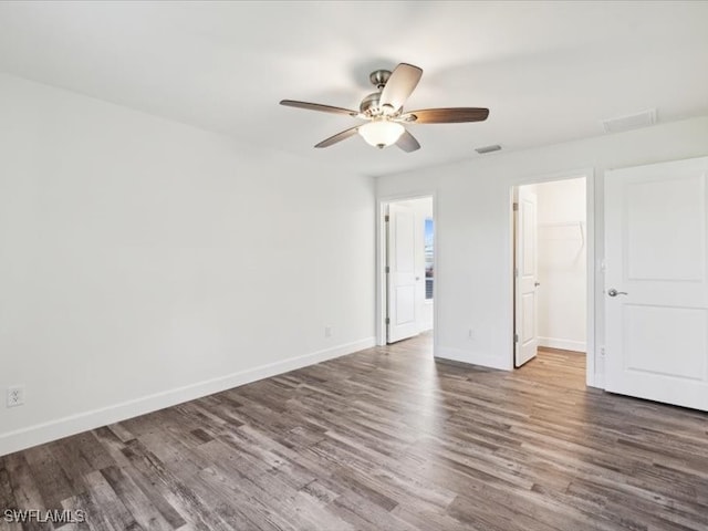 unfurnished bedroom featuring ceiling fan, a walk in closet, a closet, and dark hardwood / wood-style floors