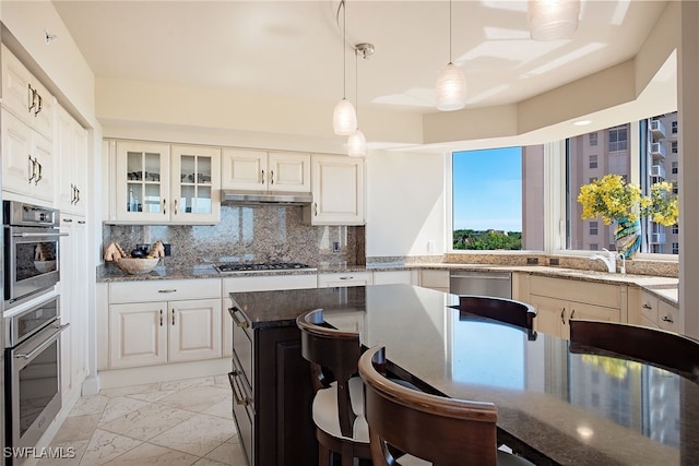 kitchen with a breakfast bar area, backsplash, appliances with stainless steel finishes, decorative light fixtures, and dark stone countertops