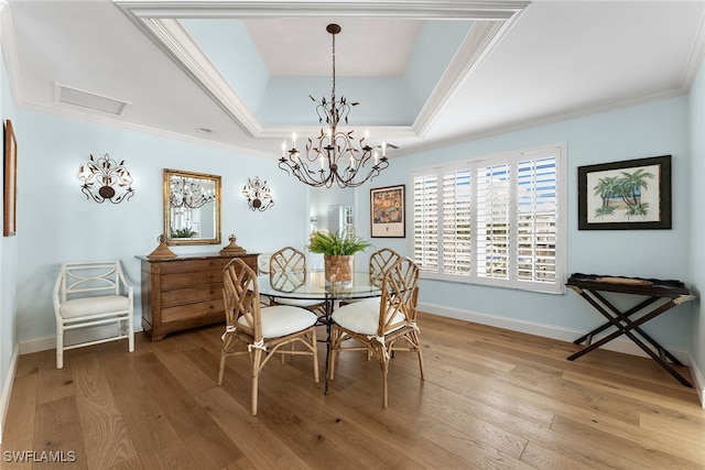 dining space featuring crown molding, a notable chandelier, light wood-type flooring, and a raised ceiling